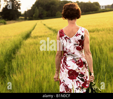 woman walking across corn field carrying bunch of roses Stock Photo