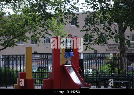A boy standing at the top of a sliding board in a New York City playground. Stock Photo