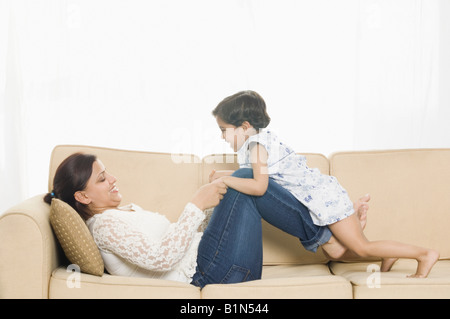 Side profile of a mid adult woman with her daughter playing on a couch Stock Photo