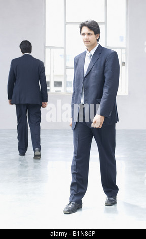 Businessman walking in an office with an another businessman in the background Stock Photo