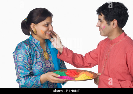 Side profile of a mid adult man applying powder paint on a mid adult woman's face Stock Photo