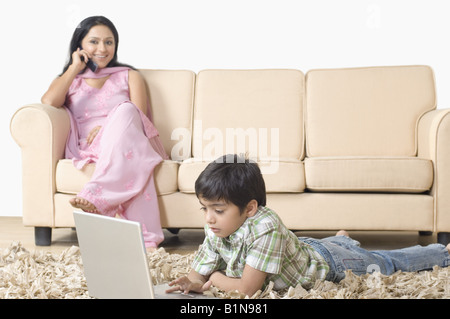 Boy using a laptop and mother talking on a mobile phone Stock Photo