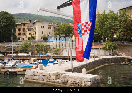 Lovran Istria Croatia Europe Croatian flag flying above jetty in small fishing port harbour for ancient fortified town on coast Stock Photo