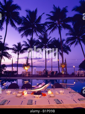 Elegant outdoor dining setup by a pool with palm trees and sunset in a tropical location Stock Photo