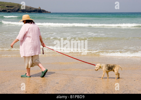 Mature woman wearing a hat and walking her very old dog along the beach at Harlyn Bay Cornwall England Stock Photo