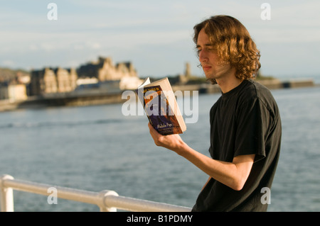Young man reading  'Last Tango in Aberystwyth' by Malcolm Price on the promenade in Aberystwyth, summer evening, Wales UK Stock Photo