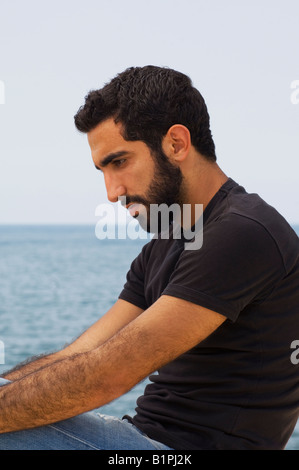 Young Arabic Muslim man sitting outdoors thinking Stock Photo