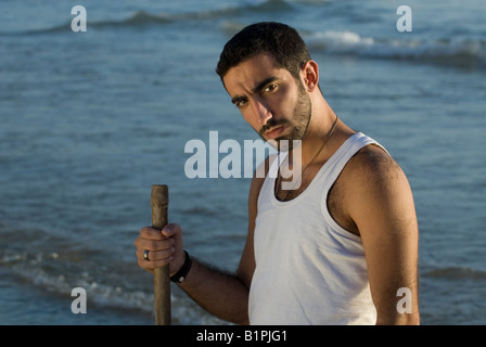 Portrait of a young Middle Eastern man standing on the beach holding a stick looking at the camera Stock Photo