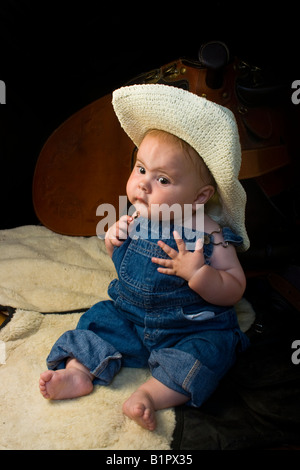 Little baby boy dressed like a cowboy sitting in front of saddle Stock Photo
