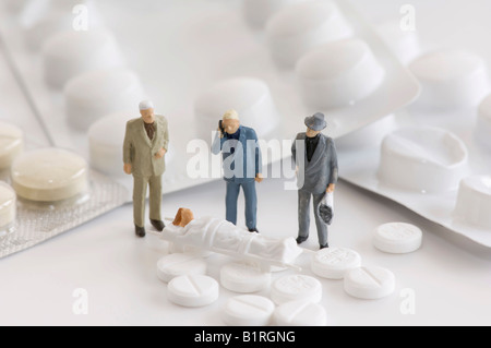 Tablets, blister packs and three miniature men standing next to a woman on a stretcher, symbolic photo Stock Photo