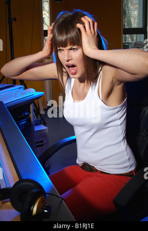Young woman sitting at a mixer in a recording studio, horror-strickenly tearing at her hair