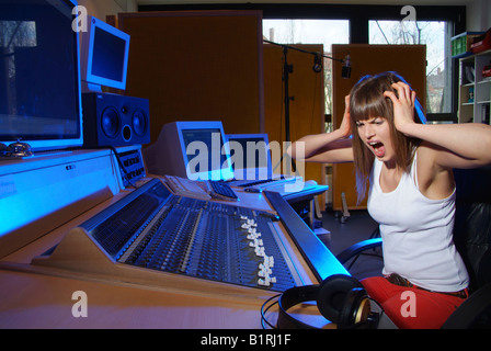 Young woman sitting at a mixer in a recording studio, angrily tearing at her hair Stock Photo