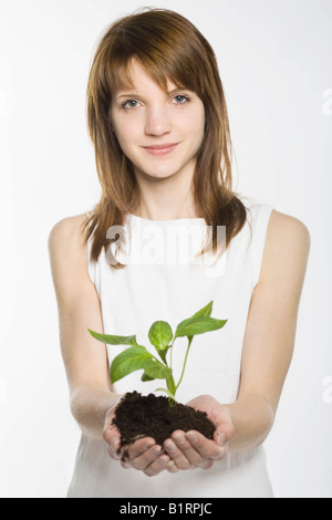 Young woman cupping a young plant rooted in soil in her hands Stock Photo