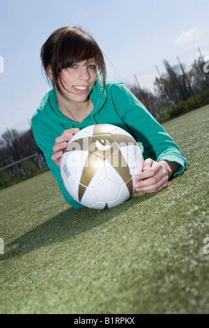 Young woman lying with a football in front of her on a football pitch Stock Photo