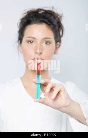 Young woman wearing a white laboratory smock holding a syringe filled with red liquid in her hand Stock Photo