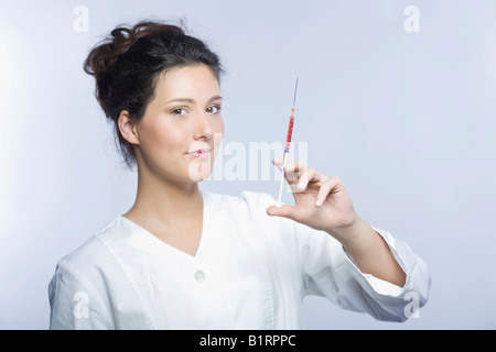 Young woman wearing a white laboratory smock holding a syringe filled with red liquid in her hand Stock Photo