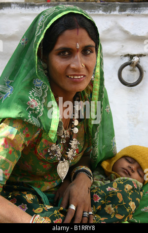 Portrait of a beautiful Rajasthani woman in a decorated green sari holding sleeping baby in Udaipur Stock Photo