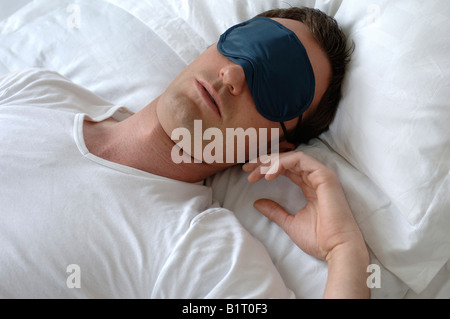 Man sleeping in bed, wearing a sleep mask Stock Photo
