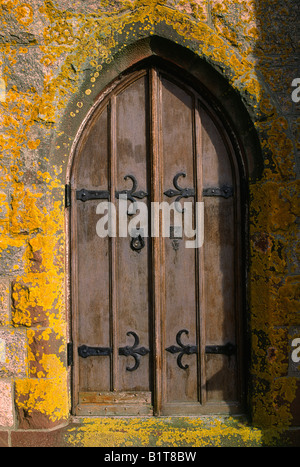 Lichen covered stone wall, arched wooden doorway to a Catholic church, Brittany, France Stock Photo