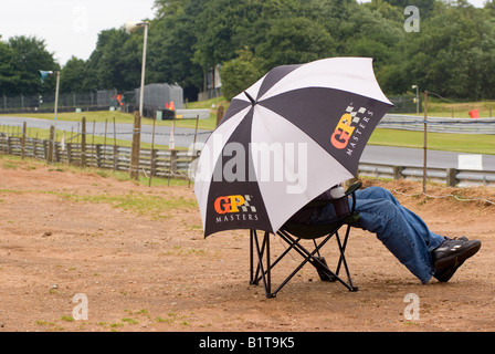 Spectator Overlooking the Avenue Sitting Under Umbrella at Oulton Park Motor Racing Circuit Cheshire England United Kingdom UK Stock Photo