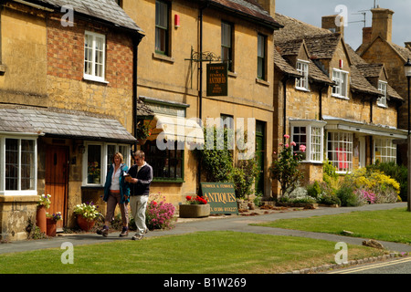 Broadway a northern Cotswold town in Worcestershire England UK Walkers passing an antiques shop Stock Photo