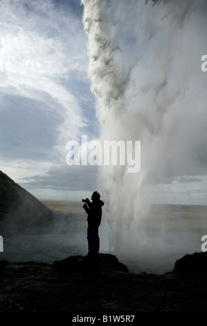 Man Taking Photo from Behind Seljalandsfoss Waterfall, Iceland Stock Photo