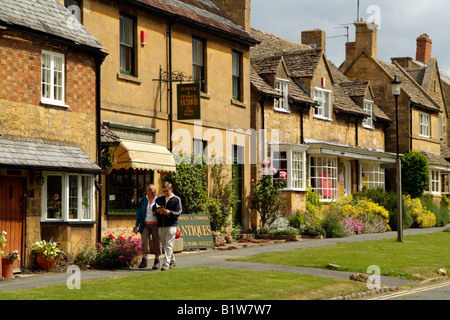 Broadway a northern Cotswold town in Worcestershire England UK Walkers passing an antiques shop Stock Photo