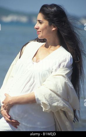 ethnic pregnant woman standing on the beach in profile Stock Photo
