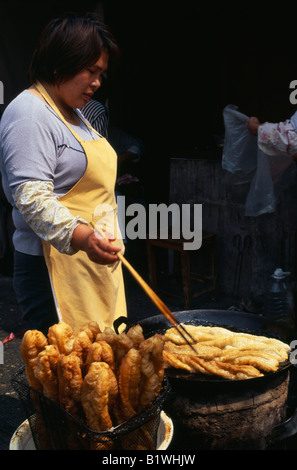 CHINA Shanghai Woman at street stall using long pair of chopsticks to turn frying food in large shallow pan wok in front of her Stock Photo