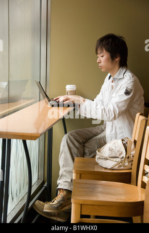 Kyoto, Japan. A young man working on a laptop computer using the free wifi in a branch of Starbucks coffee shop Stock Photo