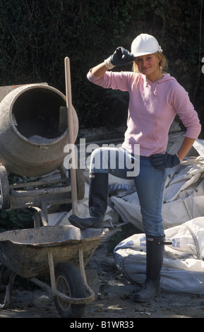 young female builder standing by cement mixer Stock Photo