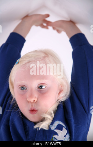 Little blonde haired school girl stretching her arms up above her head against a white background Stock Photo