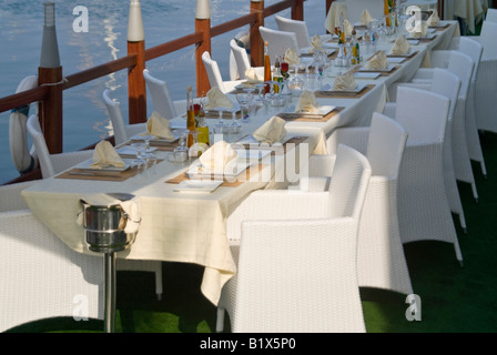 Horizontal view of a long empty table for a large party outside ready for dinner service at an expensive waterside restaurant Stock Photo