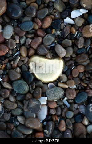 Golden heart shaped pebble amongst pebbles on a beach. Findhorn beach, Moray, Scotland Stock Photo