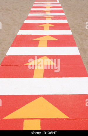 Walkway on beach painted red and white with yellow arrows Stock Photo