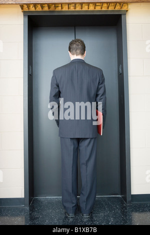 Rear view of a businessman waiting for the elevator in an office building Stock Photo