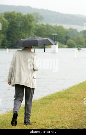 A man holding an umbrella during a brief summer rainfall walking along the River Thames at Henley Regatta week Stock Photo