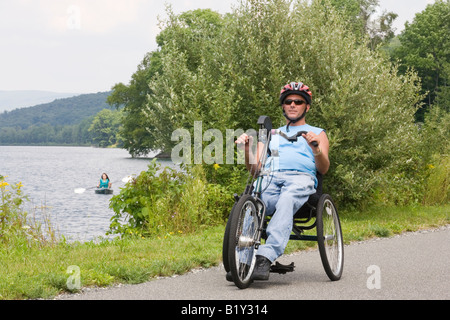 Young man riding adaptive bike with a young woman kayaking in a lake in the background Stock Photo