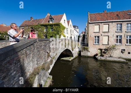 Couple taking pictures on a stone bridge over a canal in the old town, Bruges Belgium Stock Photo