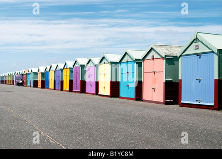 Woman sitting outside a row of colourful beachhuts on the seafront in Hove Stock Photo