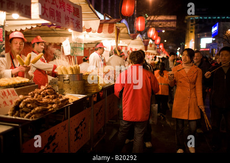 Shoppers pass stalls selling meat kebabs and corn on the cobs in the Night Market Wangfujing Street Beijing China Stock Photo