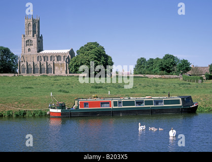 Rural riverside landscape Fotheringhay village church St Mary & All Saints moored narrowboat on River Nene swan & cygnets Northamptonshire England UK Stock Photo