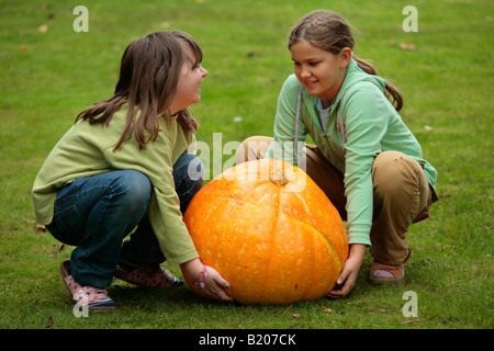 two little girls trying to lift a very big pumpkin Stock Photo