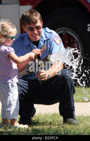 A firefighter and a young girl using a fire hose Stock Photo