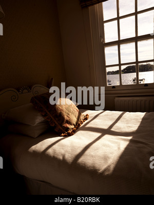 Sunlight streaming in through sash type window onto a bed with cushion.High resolution image shot on Hasseldlad 39Mp camera Stock Photo