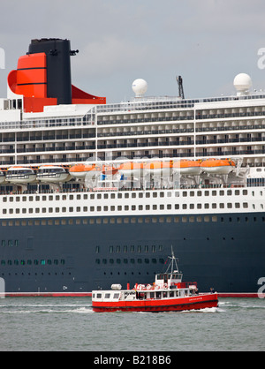 The Hythe Ferry is dwarfed by the huge Cunard transatlantic liner Queen Mary 2 while docked in Southampton Hampshire England Stock Photo