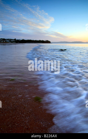 The breaking dawn on the foreshore at Goodrington Sands in South Devon with the dawn light reflecting on the breaking waves Stock Photo