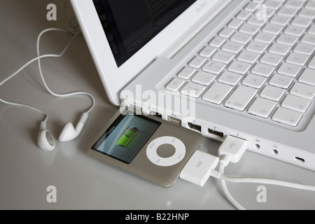 Apple ipod Nano 3rd generation MP3 player connected to white MacBook laptop computer USB port to charge battery Stock Photo
