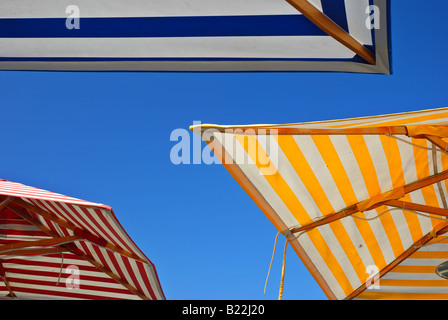 Three picnic table umbrellas in different colors outdoors set against a clear blue sky Stock Photo