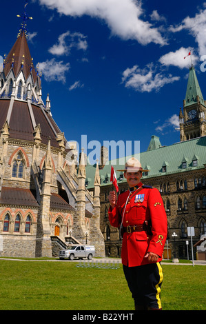 RCMP Royal Canadian Mounted Police officer holding flag at Parliament buildings Center Block and Library with Peace Tower in Ottawa Stock Photo